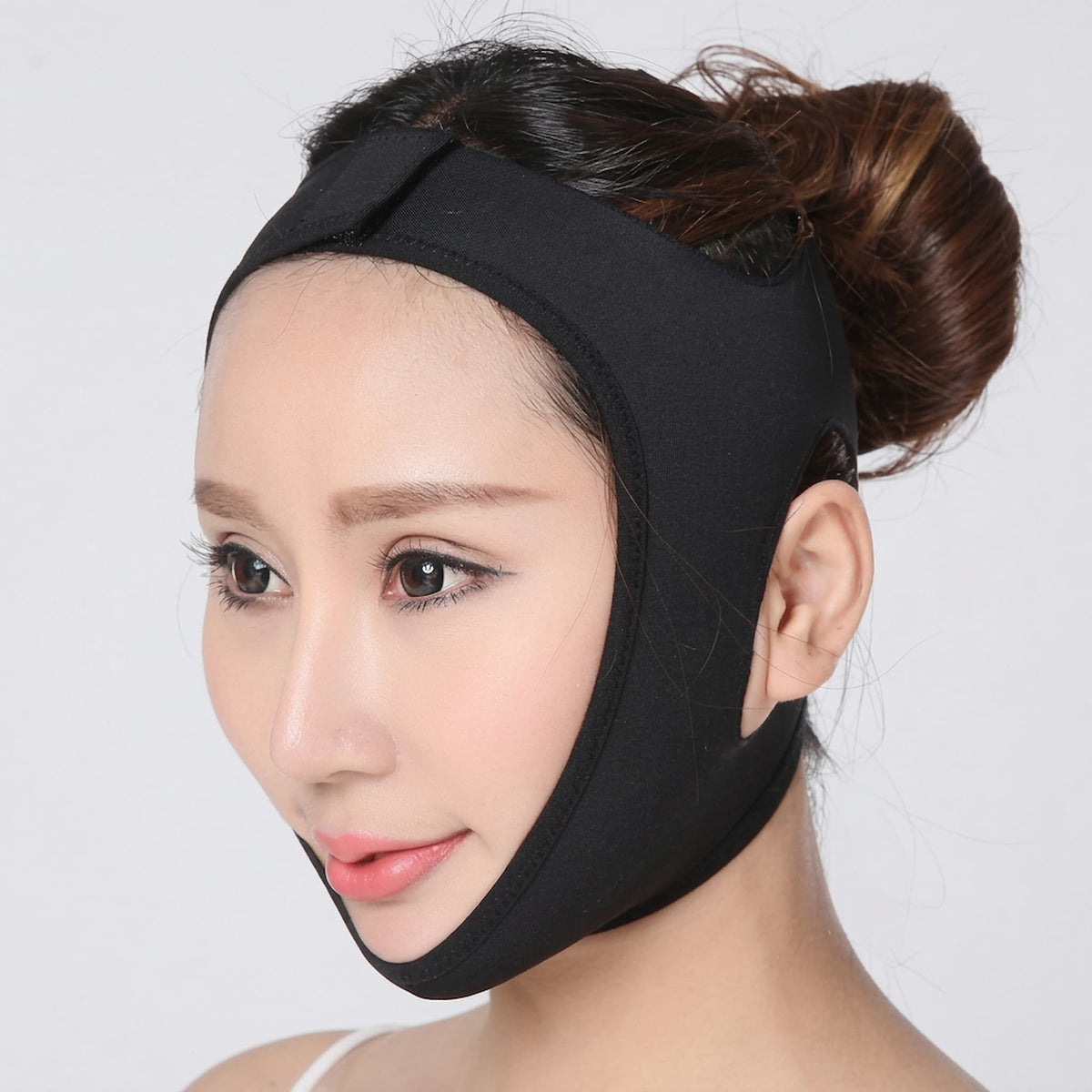 A woman wearing an elastic face lifting bandage, shown in a close-up profile against a light gray background.
