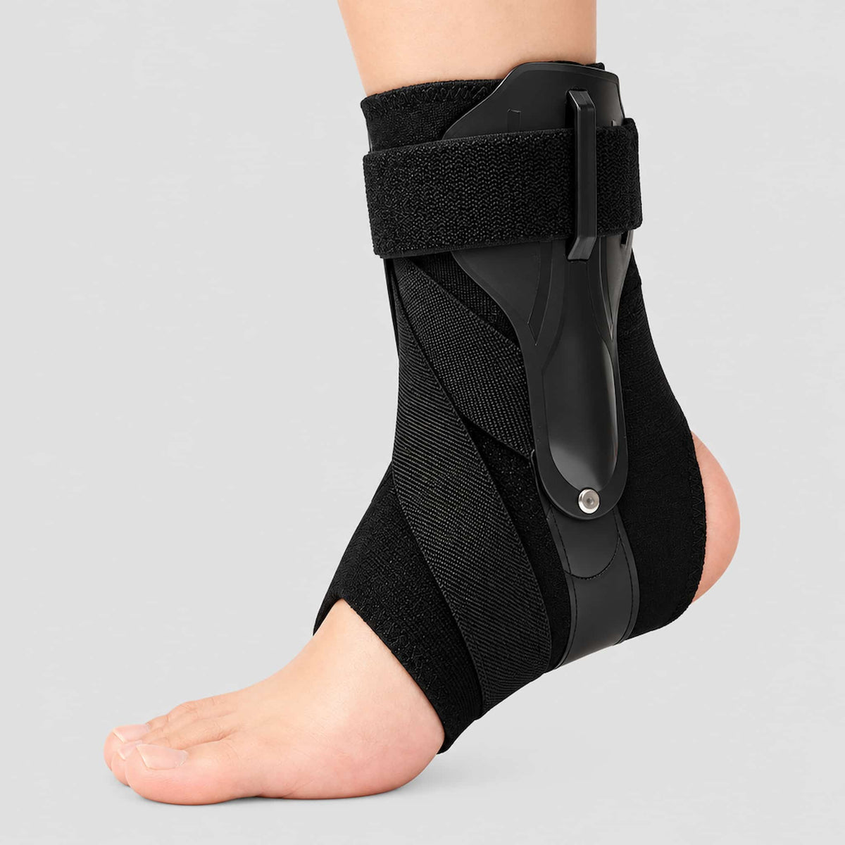 A black ankle support strap with a hook-and-loop strap and molded plastic shell, shown worn on a person's ankle against a light gray background.