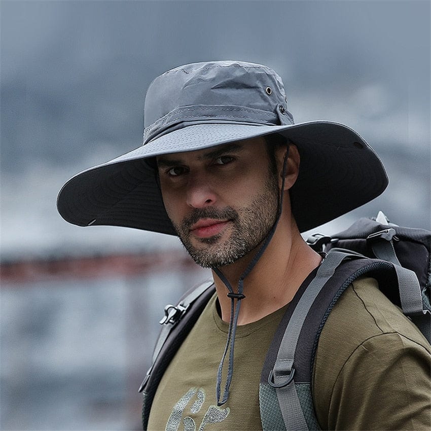 An active male hiker wearing a gray UPF 50+ sun hat looking out over a mountain trail on a bright, sunny day.