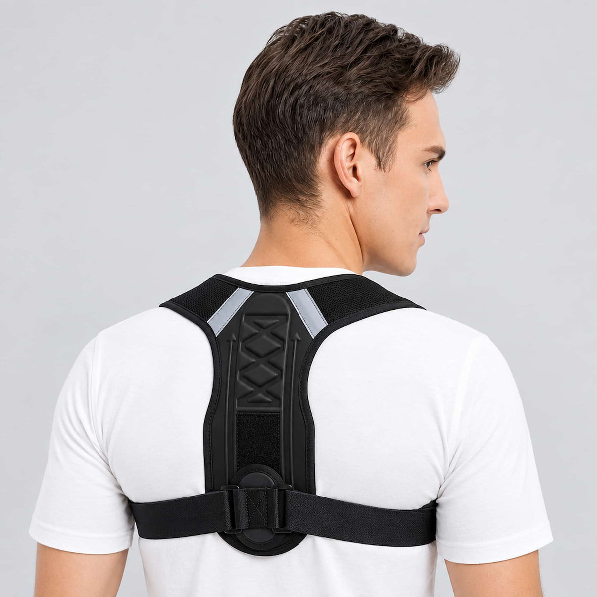 A man viewed from the back wearing an adjustable posture corrector, set against a plain light gray studio background.