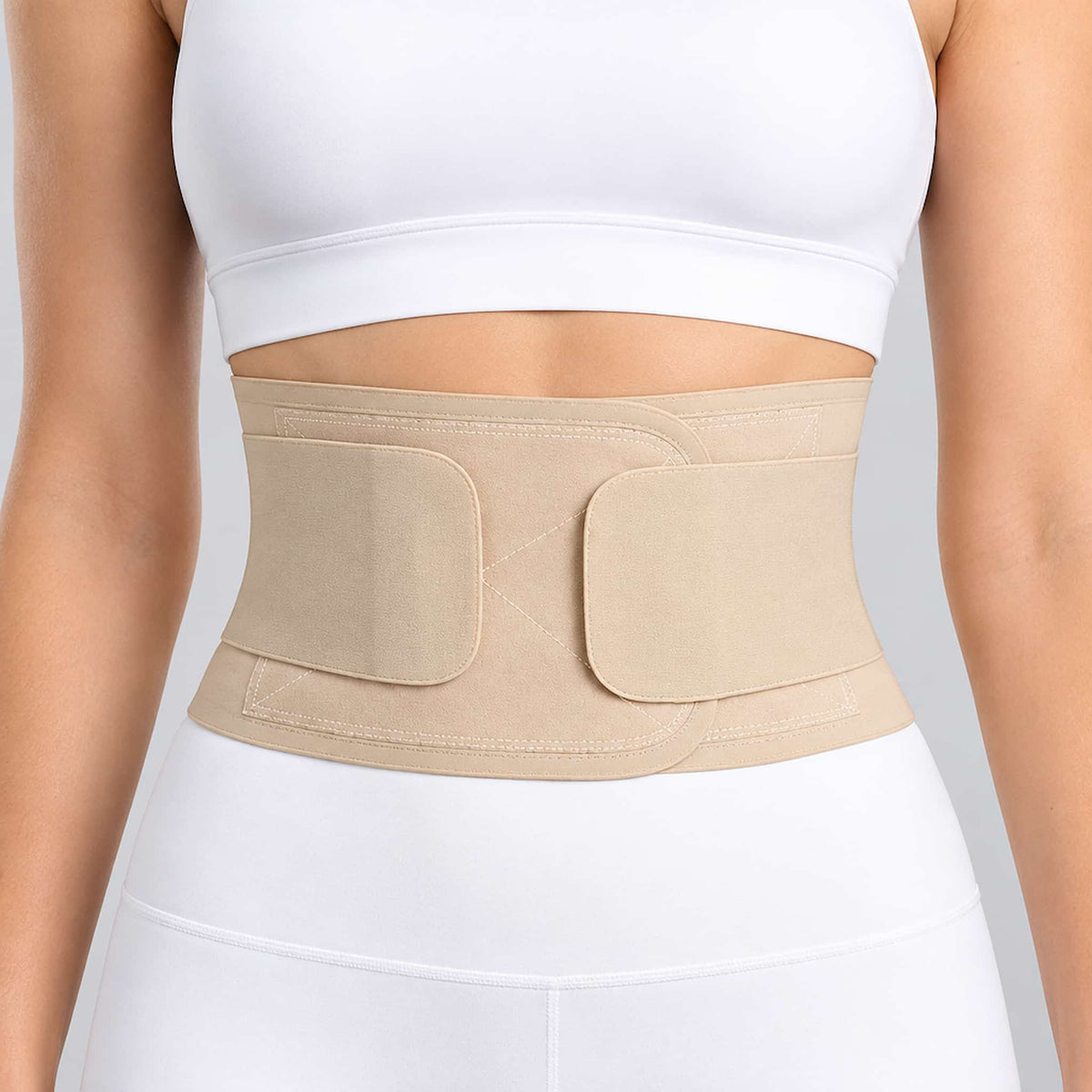 A beige back support belt for work worn by a model, shown from the chest to the hips. The model is wearing a white sports bra and white leggings against a clean white background.