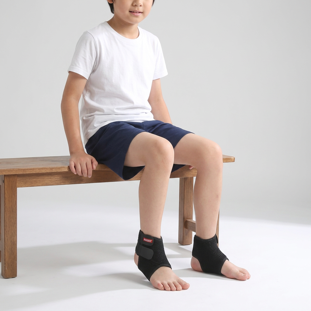 Child seated on a bench wearing black kids ankle support wraps with charcoal adjustable tabs and exposed heels and toes.