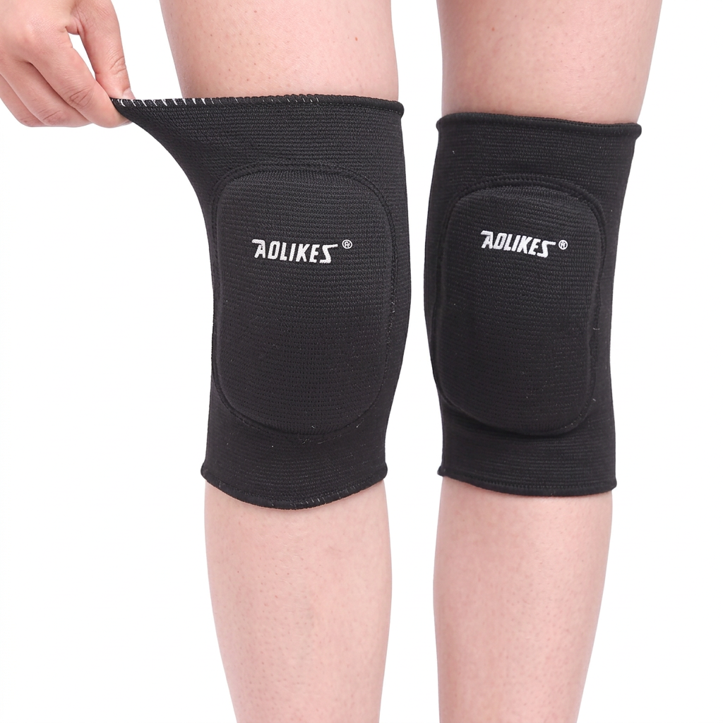 Black child knee pad sleeves with rounded padded panels, shown from the front with a hand stretching one cuff.