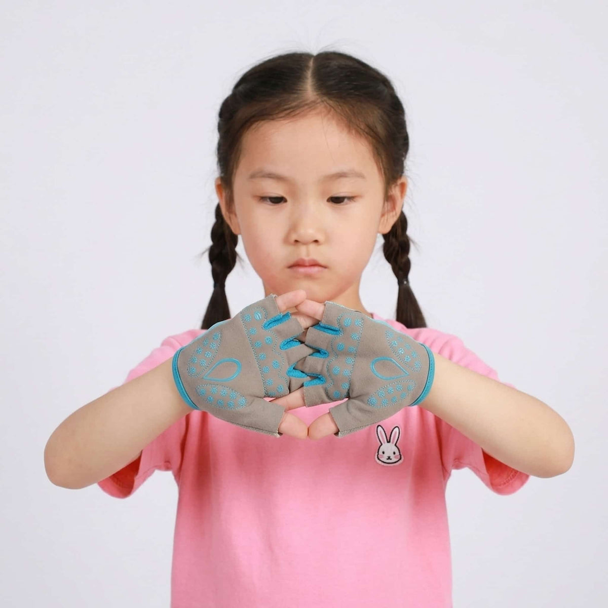 A young girl with braided hair wearing kids cycling gloves against a light gray background.