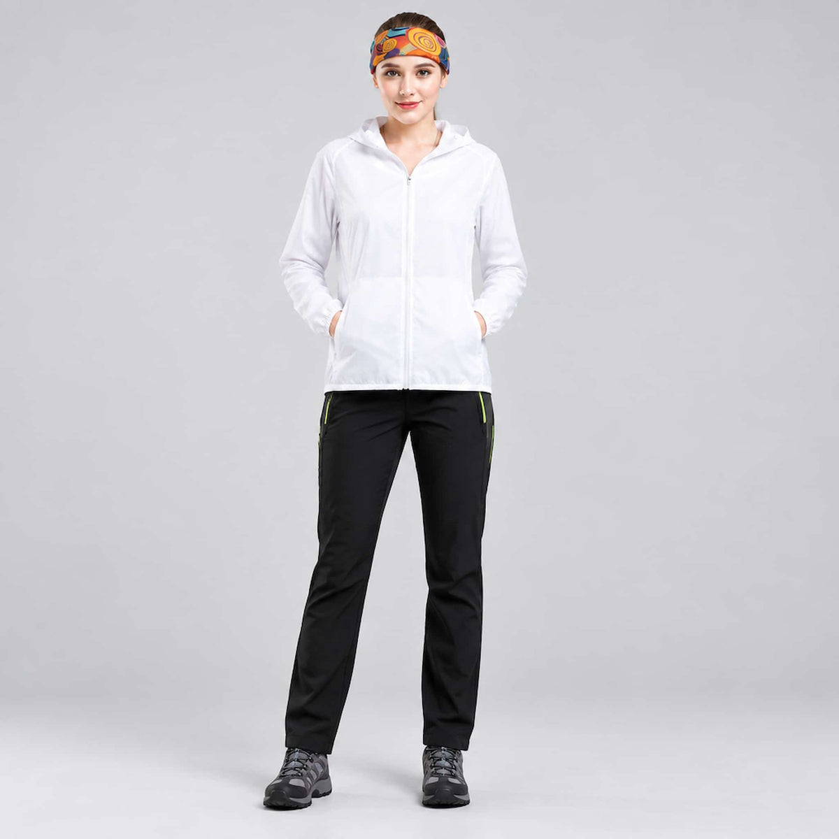 A woman modeling a packable jacket for backpacking and travel, standing against a neutral gray studio background.