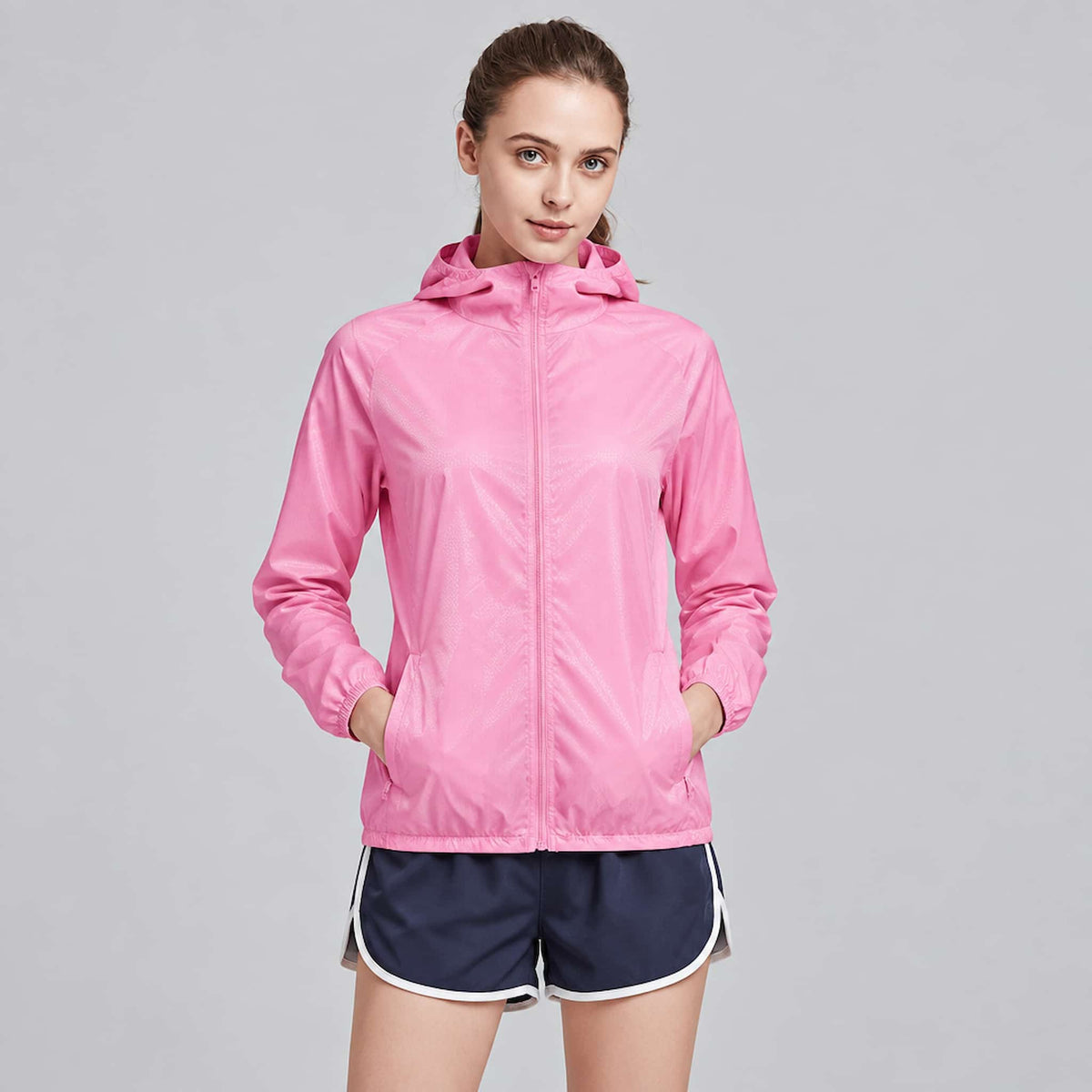 A woman modeling a packable nylon jacket for hiking against a plain light gray studio background.