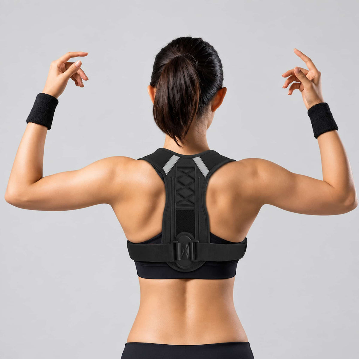 A woman viewed from behind wearing a posture corrector for men and women, against a plain light gray studio background.