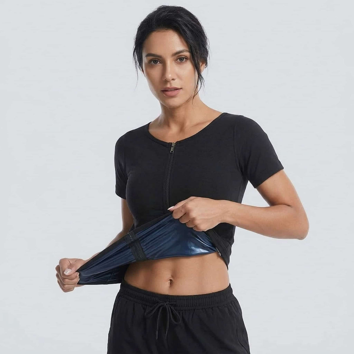 A woman modeling a sweat enhancer body shaper against a light gray studio background.