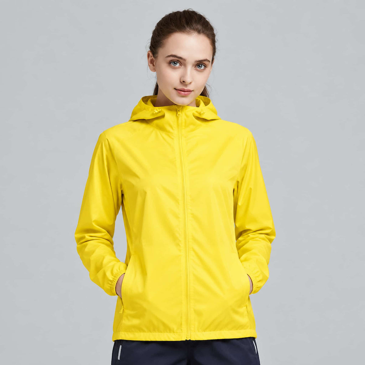 A woman wearing a water-repellent windbreaker jacket, standing against a solid light gray studio background.