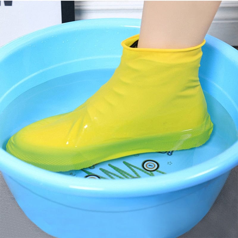 A pair of yellow plastic shoe covers fitted on a human foot, standing in a blue bucket filled with water.